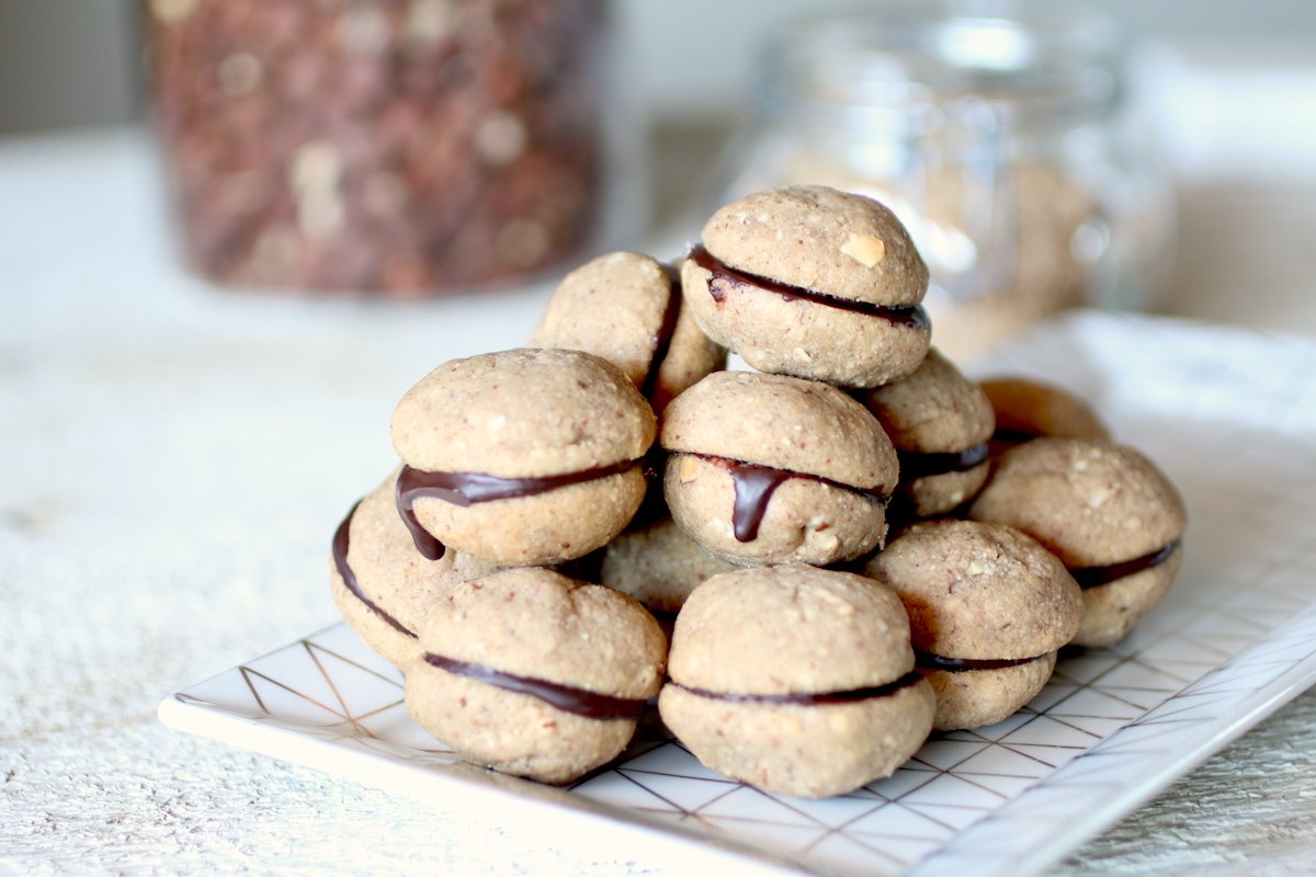 baci di dama con il cioccolato che gocciola su un vassoio e nocciole sullo sfondo