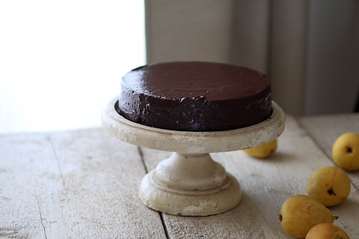 Torta al cioccolato sull'alzata di legno con le pere sul tavolo