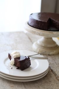 Torta al cioccolato glassata sull'alzata e una fetta appena tagliata e servita con la panna