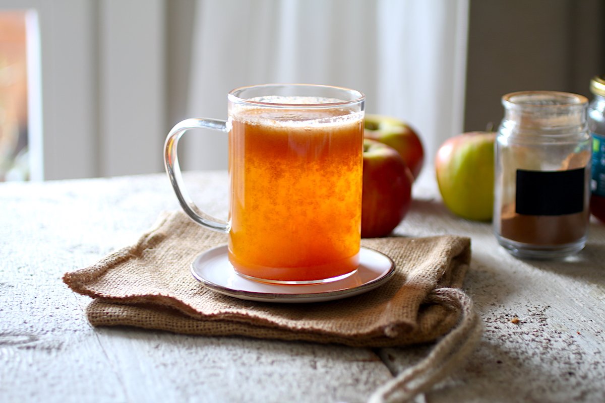 Una tazza trasparente con il succo di mele su un tavolo di legno